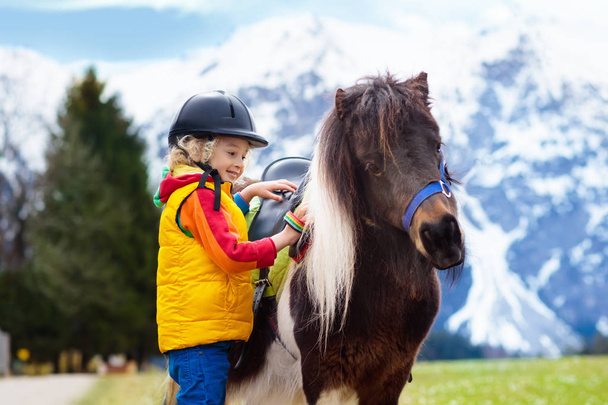 Miúdos a montar pónei. Criança a cavalo nas montanhas dos Alpes
 - Foto, Imagem