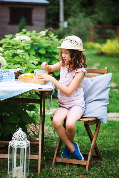 happy child girl drinking tea with lemons in summer garden in the morning.  - Photo, Image