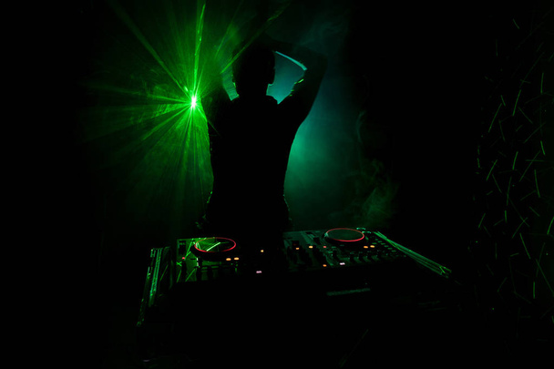 DJ dreht, mischt und kratzt in einem Nachtclub, Hände von DJ zwicken verschiedene Track-Controller auf dem Deck, Blitzlicht und Nebel, oder DJ mischt den Track im Nachtclub bei Party. Selektiver Fokus - Foto, Bild