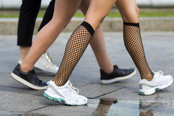 Três pares de jovens pernas slim fit meninas em diferentes sapatos esportivos andando rápido ao longo da estrada de concreto.
. - Foto, Imagem