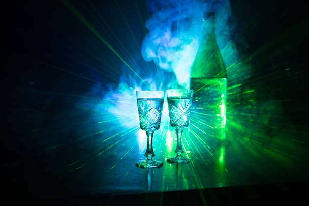 İki kadeh votka şişesiyle karanlık sisli parlayan ışıklar (lazer, Stobe) çok renkli stil arka plan kulübü. Kulüp tema dekorasyon içer. Boş alanı. Seçici odak - Fotoğraf, Görsel