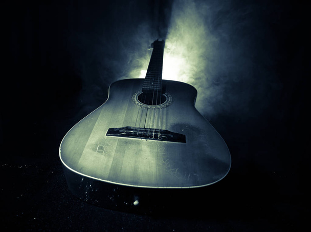 Muziek concept. Akoestische gitaar op een donkere achtergrond onder lichtstraal met rook. Gitaar met de snaren, close-up. Selectieve aandacht. Effect van brand. - Foto, afbeelding