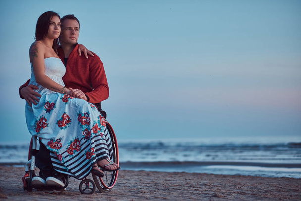 Una pareja amorosa, una mujer se sienta en su regazo maridos, descansando en una playa sobre un fondo de un amanecer brillante
. - Foto, Imagen
