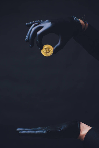 Bitcoin. Hand drops gold coin. Hands in black gloves. Concept fall crypto currency. Isolated on black background. - Фото, изображение