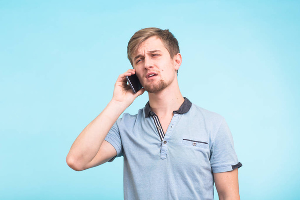 Portrait of young man talking on phone over blue background - Fotoğraf, Görsel