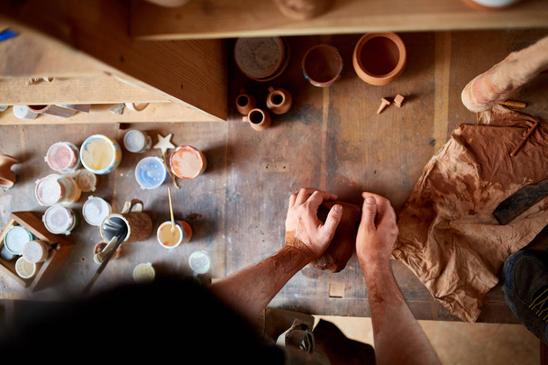 Maestro di vasaio maschio adulto che modella la piastra di argilla sulla ruota dei vasai. Vista dall'alto, primo piano, solo le mani
. - Foto, immagini