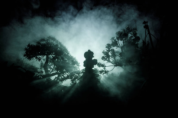 Horror Halloween decorado imagem conceitual. Sozinha com a luz na floresta à noite. Silhueta de menina de pé entre árvores com luz surreal. Foco seletivo
. - Foto, Imagem
