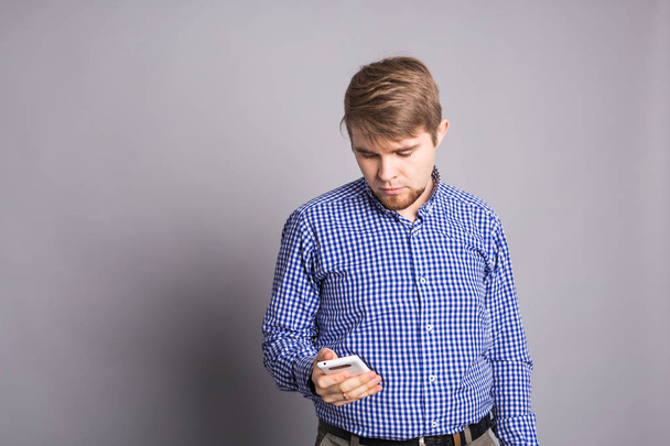 Mladý muž psaní textové zprávy na jeho mobilní telefon na šedém pozadí - Fotografie, Obrázek