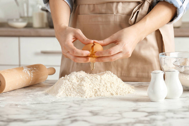 Woman breaking egg over pile of flour on table in kitchen - Foto, Imagem