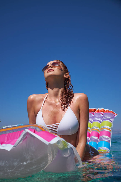 girl on the beach against a blue sunny sky. Holding a pink inflatable mattress, sunglasses, wet tanned skin. Rest, south, resort, beach. Sunny day. - Foto, Imagem