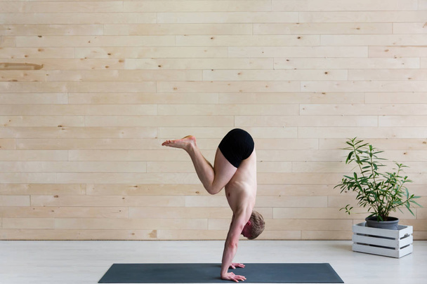Sporty man practices yoga handstand asana Adho Mukha Vrikshasana at the yoga studio. Balance exercise - Photo, Image
