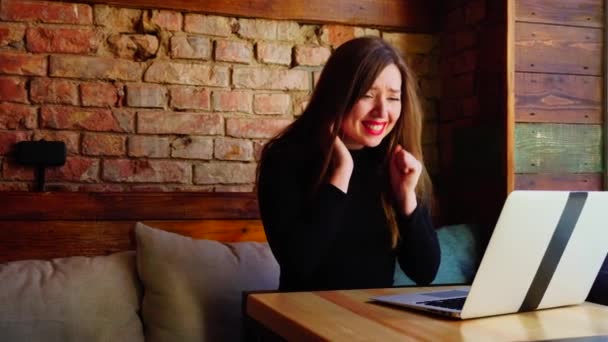 Ευτυχισμένη γυναίκα κερδισμένα στοιχήματα σε απευθείας σύνδεση με το laptop στο καφενείο κοντά σε τοίχο από τούβλα. - Πλάνα, βίντεο