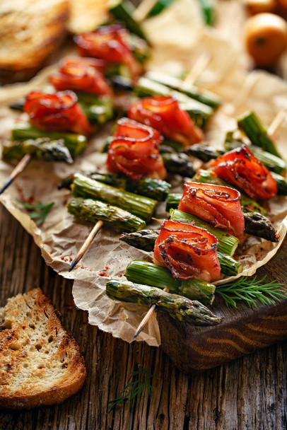 Grilled skewers with green asparagus and bacon on a wooden table. Grilled food, bbq. - Photo, Image