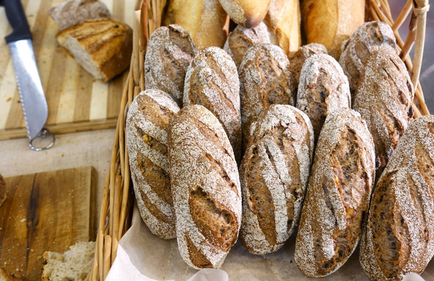 Bochenki chleba w koszu na stole obok noża, deski do krojenia chleba                                - Zdjęcie, obraz