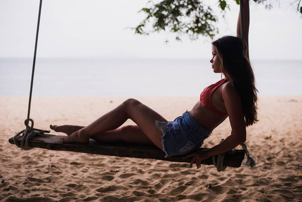 Matkustaja nainen rentouttava puinen keinu. Nuori muoti nainen rentoutua rannalla. Hyvää saaren elämäntapaa. Valkoinen hiekka, sininen pilvinen taivas ja kristallimeri trooppisella rannalla. Loma, loma
 - Valokuva, kuva