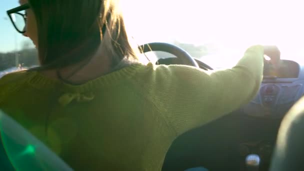 Vrouw in glazen met behulp van een smartphone in de auto, de veiligheidsgordel vastmaakt en rijdt de motor van de auto 's - Video
