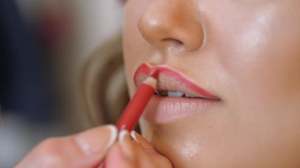 Makeup artist stylist works with model. stylist draws the contour of the models lips with a red pencil. - Кадри, відео