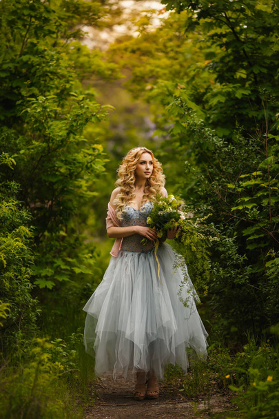 Beautiful bride in unusual dress with bouquet walking in garden - Fotoğraf, Görsel