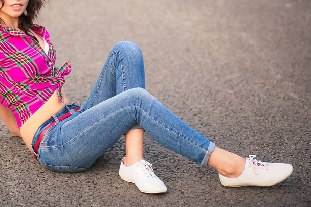 Sexy dívka s úsměvem v džínách a boty sedí na silnici - Fotografie, Obrázek