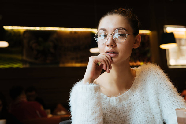 beautiful young girl in glasses sits in a cafe after work, relaxes, looks at the camera - Foto, imagen