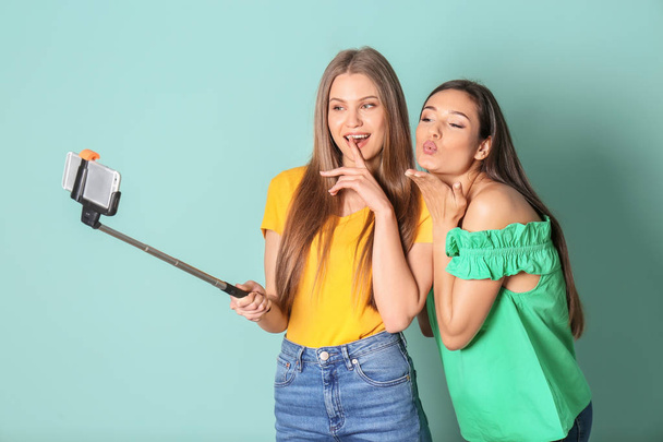 Young beautiful women taking selfie against color background - Foto, afbeelding