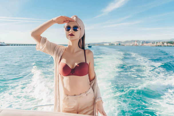 a luxurious young woman in sunglasses swims on her white yacht on the Caribbean sea, looking into the distance - Фото, изображение