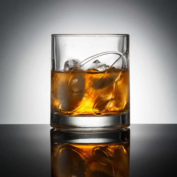 CHELYABINSK, RUSSIA - April 10,2018 Glass of Finest Blended Scotch Whiskey Ballantines Logo with natural ice cubes advertising shot on background with realistic reflection Delicious Scotch Whisky Ballantines is produced in Dambarton, Scotland by Pern - Fotó, kép