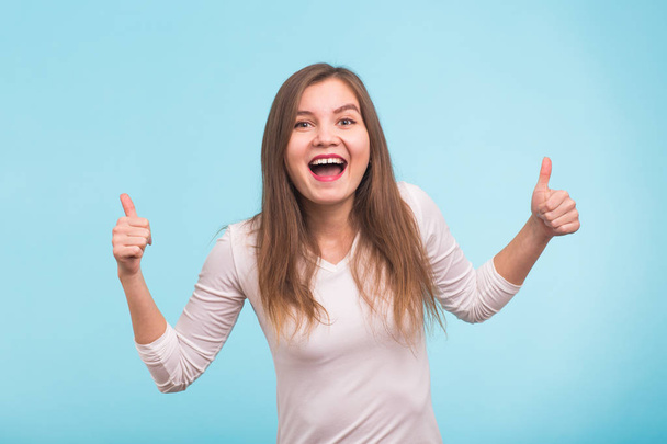 Happy young woman giving thumbs up on blue background - Foto, imagen
