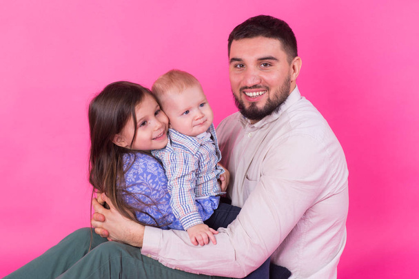 красивый отец носит свою маленькую дочь и маленького сына на розовом фоне
 - Фото, изображение