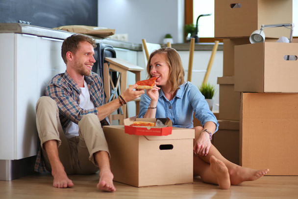Young couple have a pizza lunch break on the floor after moving into a new home with boxes around them. Young couple - Foto, Imagen
