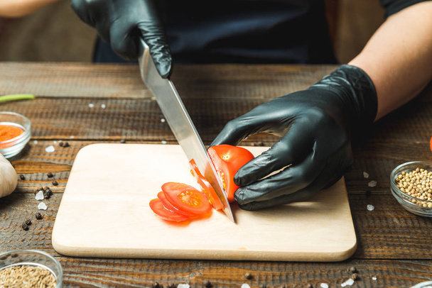 las manos de las mujeres cortan un tomate, junto a la mentira el pimentón, hierbas, pepinos y condimentos
 - Foto, Imagen