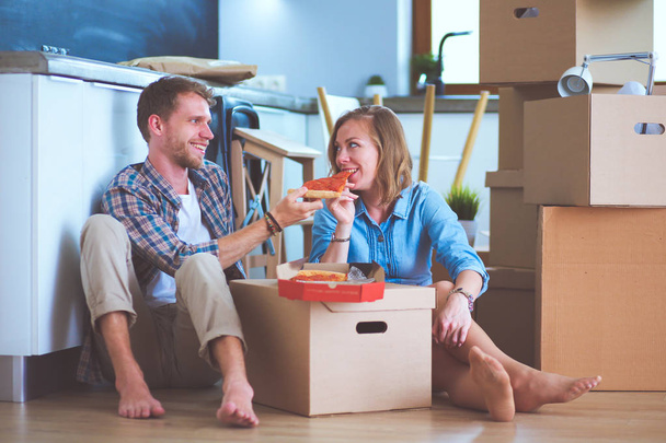 Young couple have a pizza lunch break on the floor after moving into a new home with boxes around them. Young couple - Foto, afbeelding
