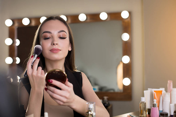 Pleasant young woman is powdering her face - Fotoğraf, Görsel