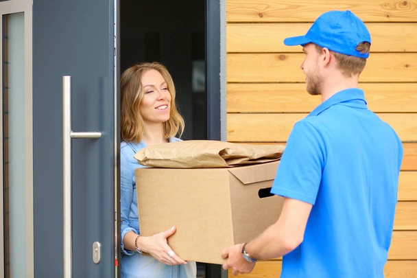 Smiling delivery man in blue uniform delivering parcel box to recipient - courier service concept. Smiling delivery man in blue uniform - Фото, изображение
