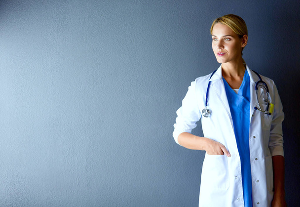 Portrait of young woman doctor with white coat standing in hospital. - Фото, изображение