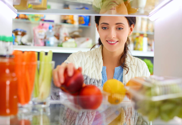 Sağlıklı yiyecek, sebze ve meyvelerle dolu açık buzdolabının yanında duran kadın portresi. Kadın portresi - Fotoğraf, Görsel