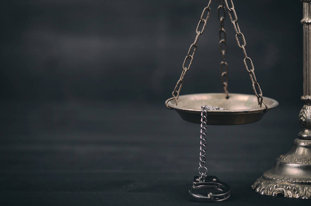 Scales of Justice and handcuffs on a black wooden background. - Foto, afbeelding