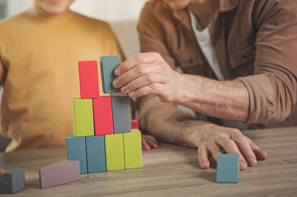 Cheerful man and boy building toy tower from cubes - Foto, Bild