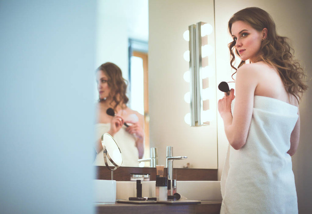 Young woman looking in the mirror and putting make-up on. - Foto, Bild