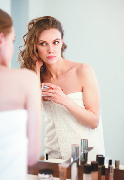 jonge vrouw kijken in de spiegel en zetten make-up op. - Foto, afbeelding