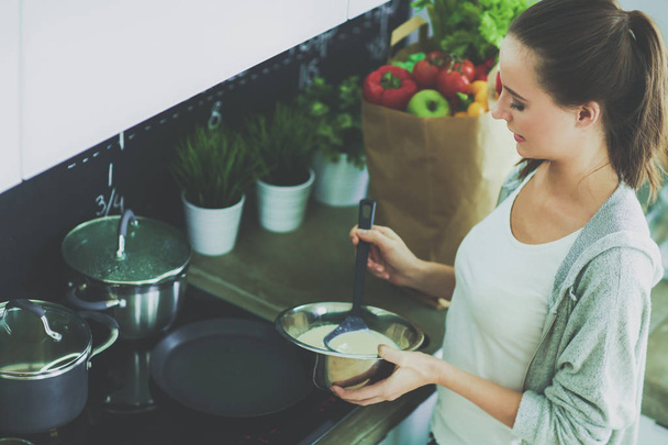 Young woman prepares pancakes in the kitchen while standing near the table. Woman in the kitchen. Cooking at kitchen. - Foto, Bild