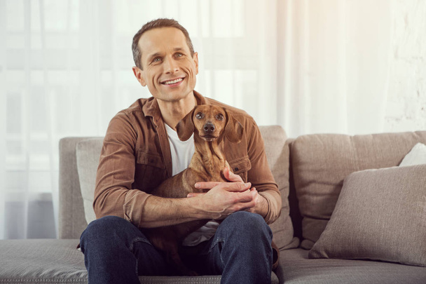 Happy man holding pet and sitting on sofa - Fotografie, Obrázek