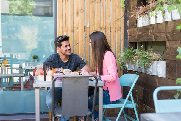 glückliches junges Paar sitzt auf einer Restaurantterrasse und isst einen Burger - Foto, Bild