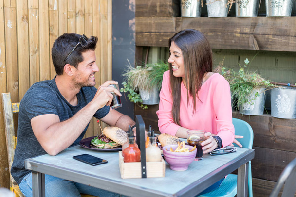 Boldog fiatal pár ülés eszik egy hamburgert étterem terasszal - Fotó, kép