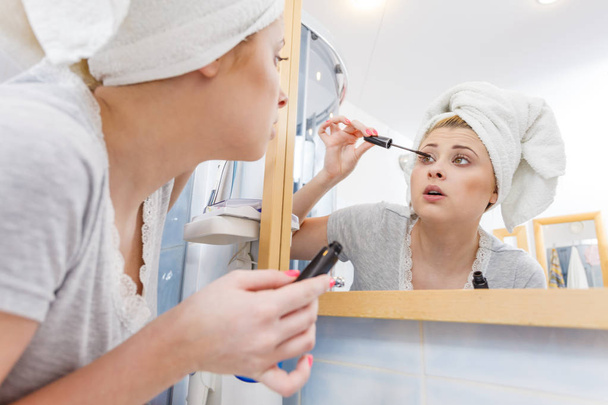 Woman in bathroom applying mascara on eyelashes - Zdjęcie, obraz