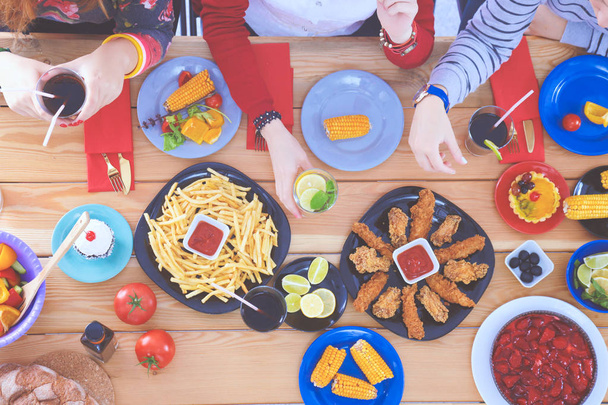 Top view of group of people having dinner together while sitting at wooden table. Food on the table. People eat fast food. - Photo, image