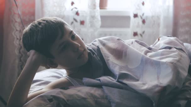 boy lies in bed, covered with a blanket before bedtime - Felvétel, videó
