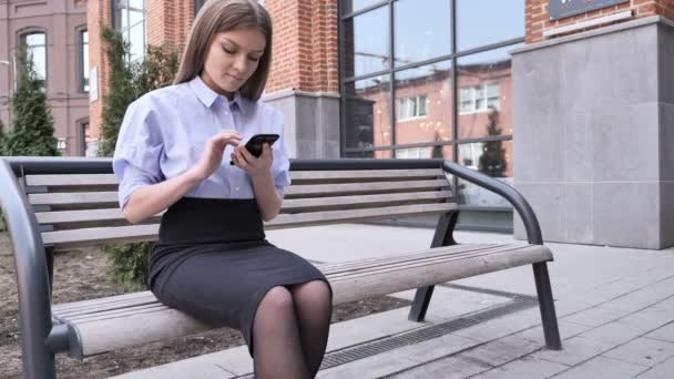 Mujer usando Smartphone, Navegando mientras está sentado fuera del edificio de oficinas
 - Metraje, vídeo