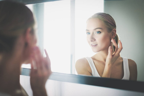 Woman caring of her beautiful skin on the face standing near mirror - Photo, image