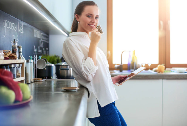 Portrait of young woman standing against kitchen background. - 写真・画像